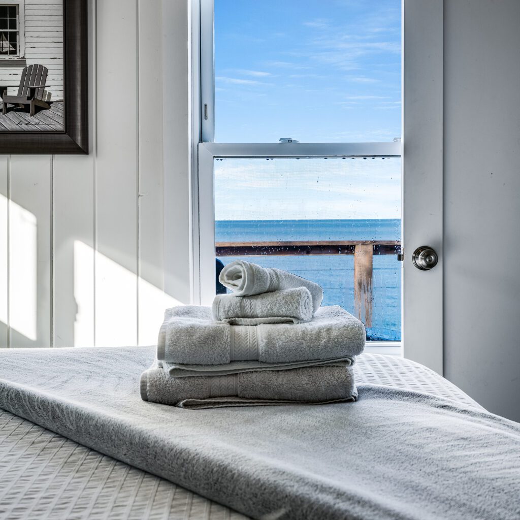 Bath towels nicely folded on the edge of the bed with a window overlooking the lake.