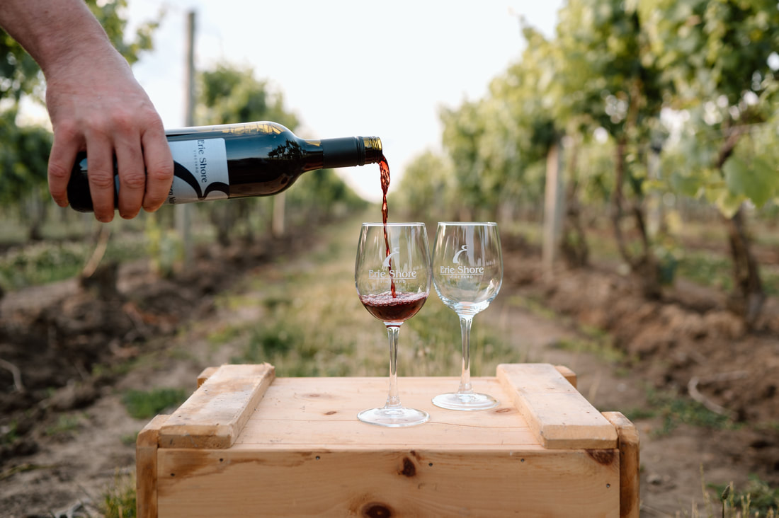 Erie Shore Winery vineyard with wine being poured into branded glasses on a crate.